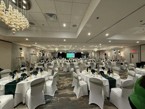 Banquet hall set for a formal event with round tables, white chair covers, and chandeliers