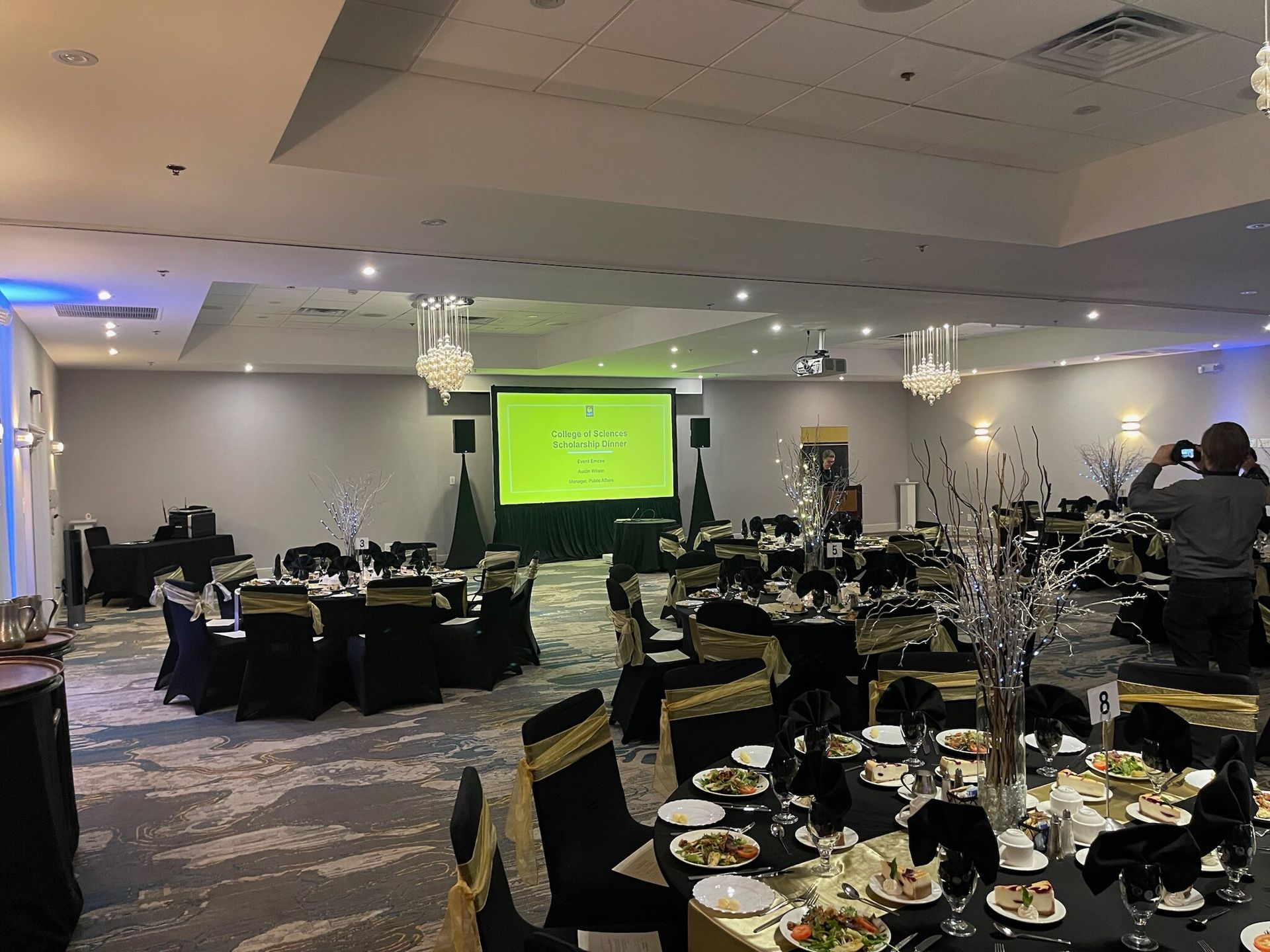 Banquet hall with round tables set for an event and a green presentation screen at the front