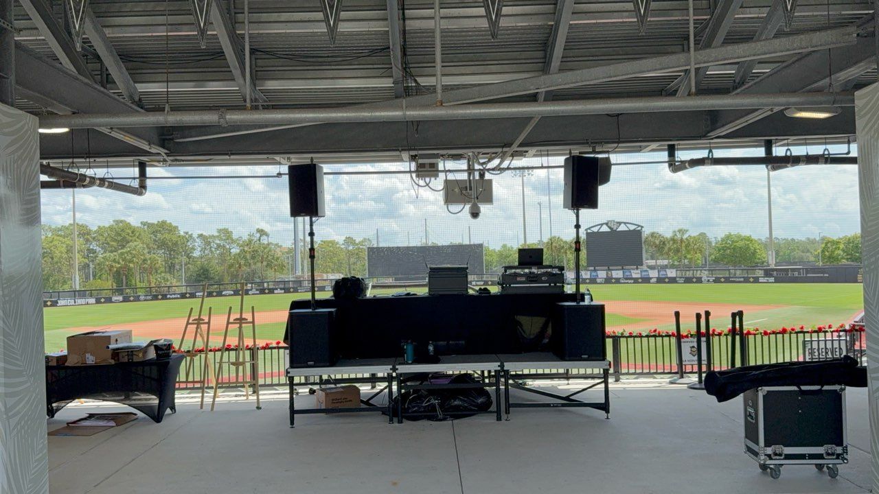 Covered outdoor stage with speakers, large screens, and a grassy field beyond the open front.