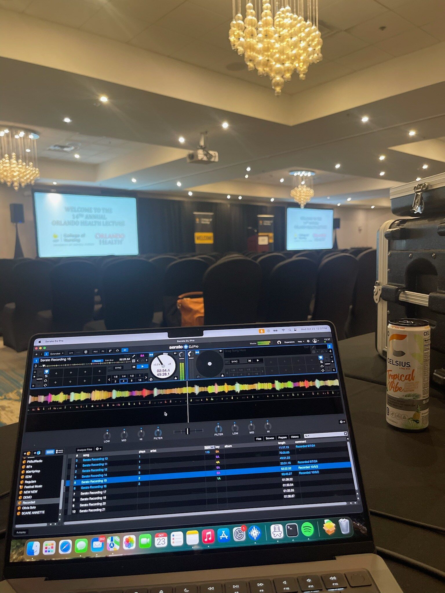 Laptop with DJ software in a banquet hall, with a crowd and two projection screens in the background
