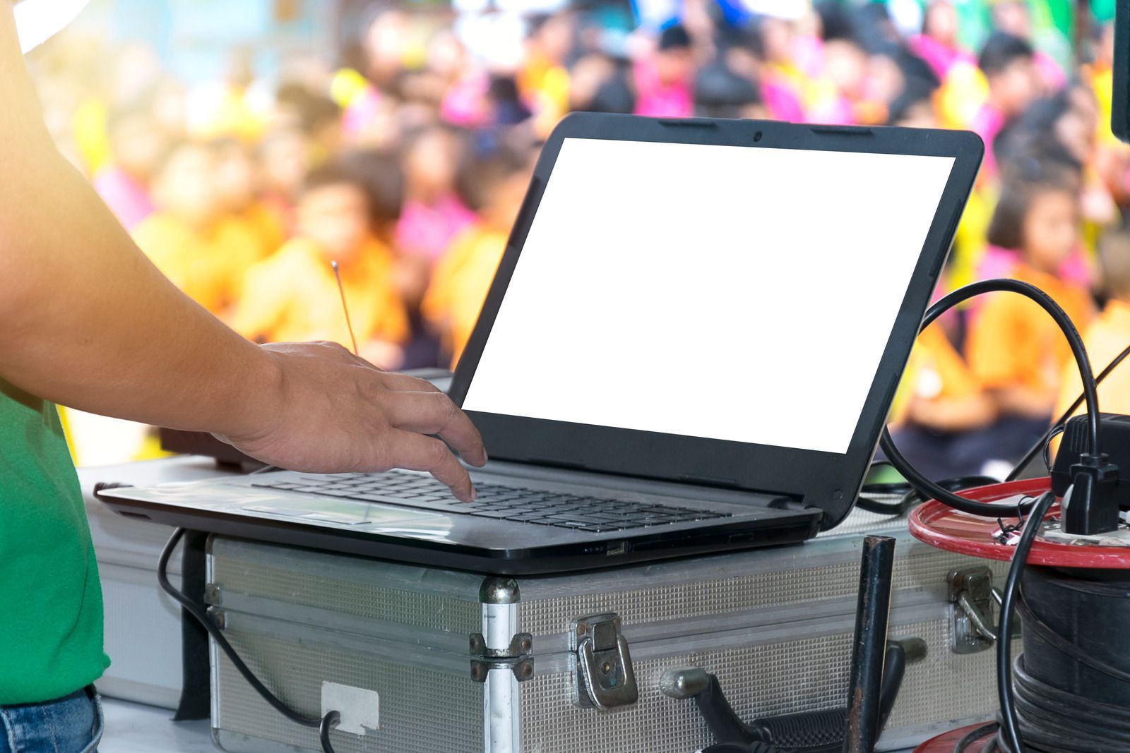 Person using a laptop on a case at an outdoor event with a colorful blurred crowd in the background