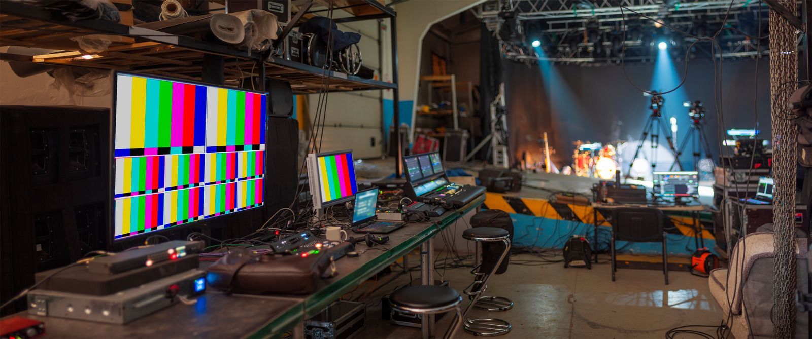 TV studio control room with monitors, mixing consoles, and a brightly lit stage set in the background