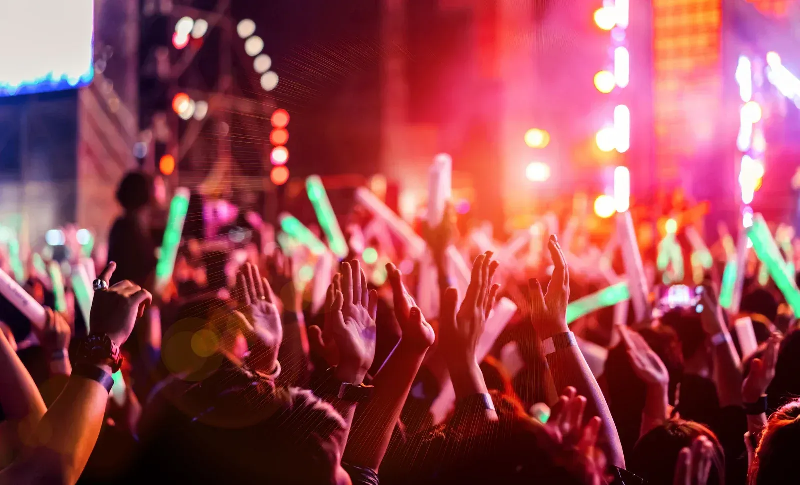 Crowd at a concert with raised hands and glowing red and green lights at night