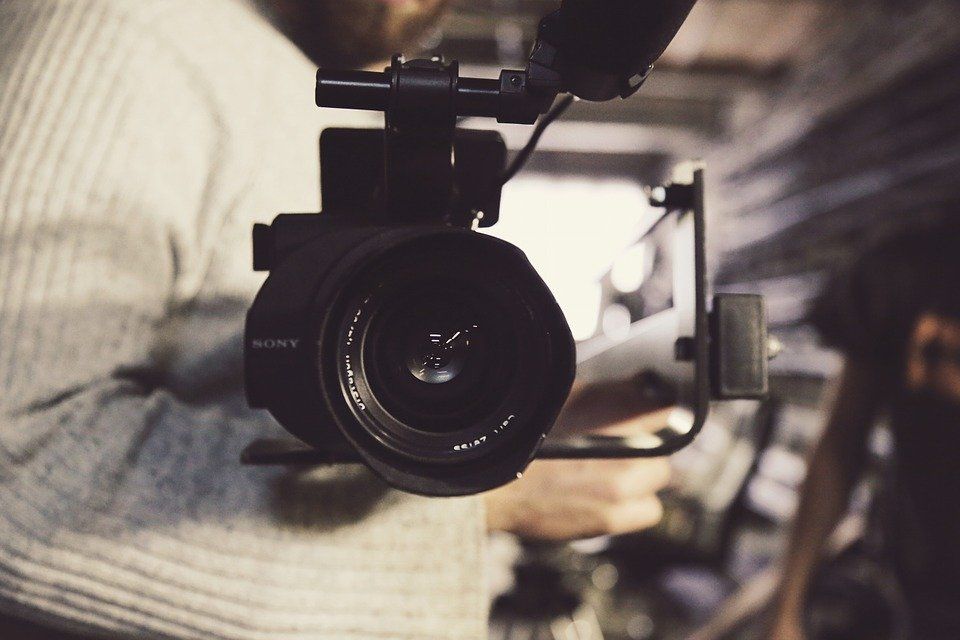 Close-up of a black camera lens held by a person in a striped shirt indoors