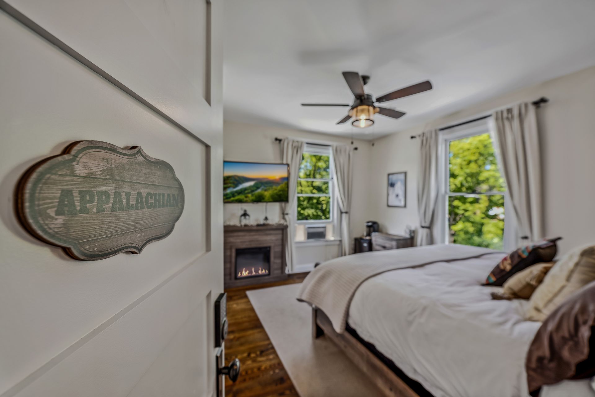 A bedroom with a king size bed , fireplace , television and ceiling fan.