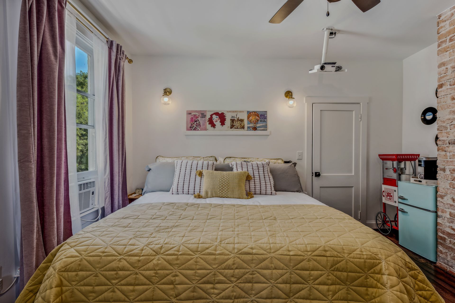 A bedroom with a bed , ceiling fan , and popcorn machine.