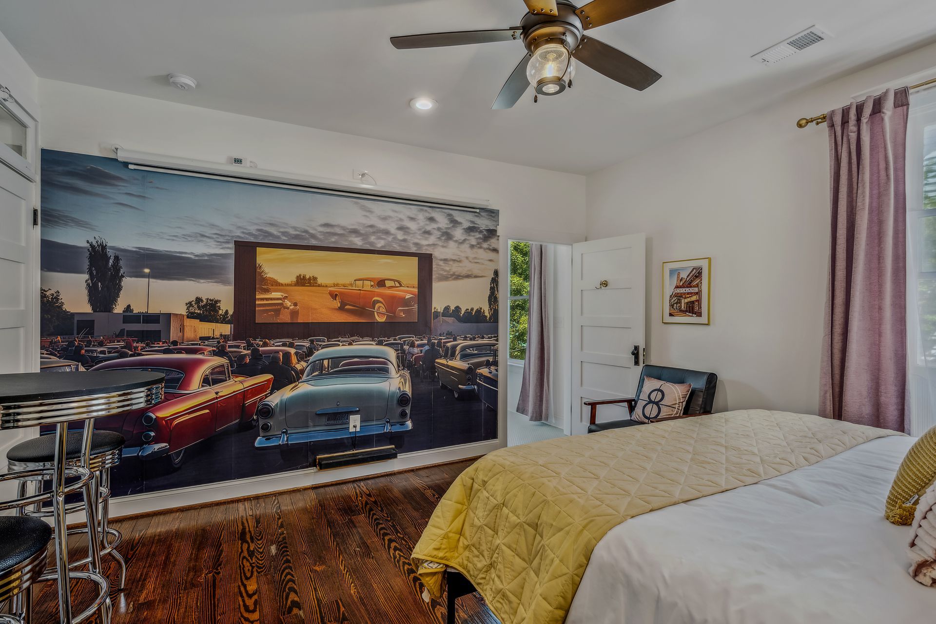 A bedroom with a bed , ceiling fan , and a picture of cars on the wall.