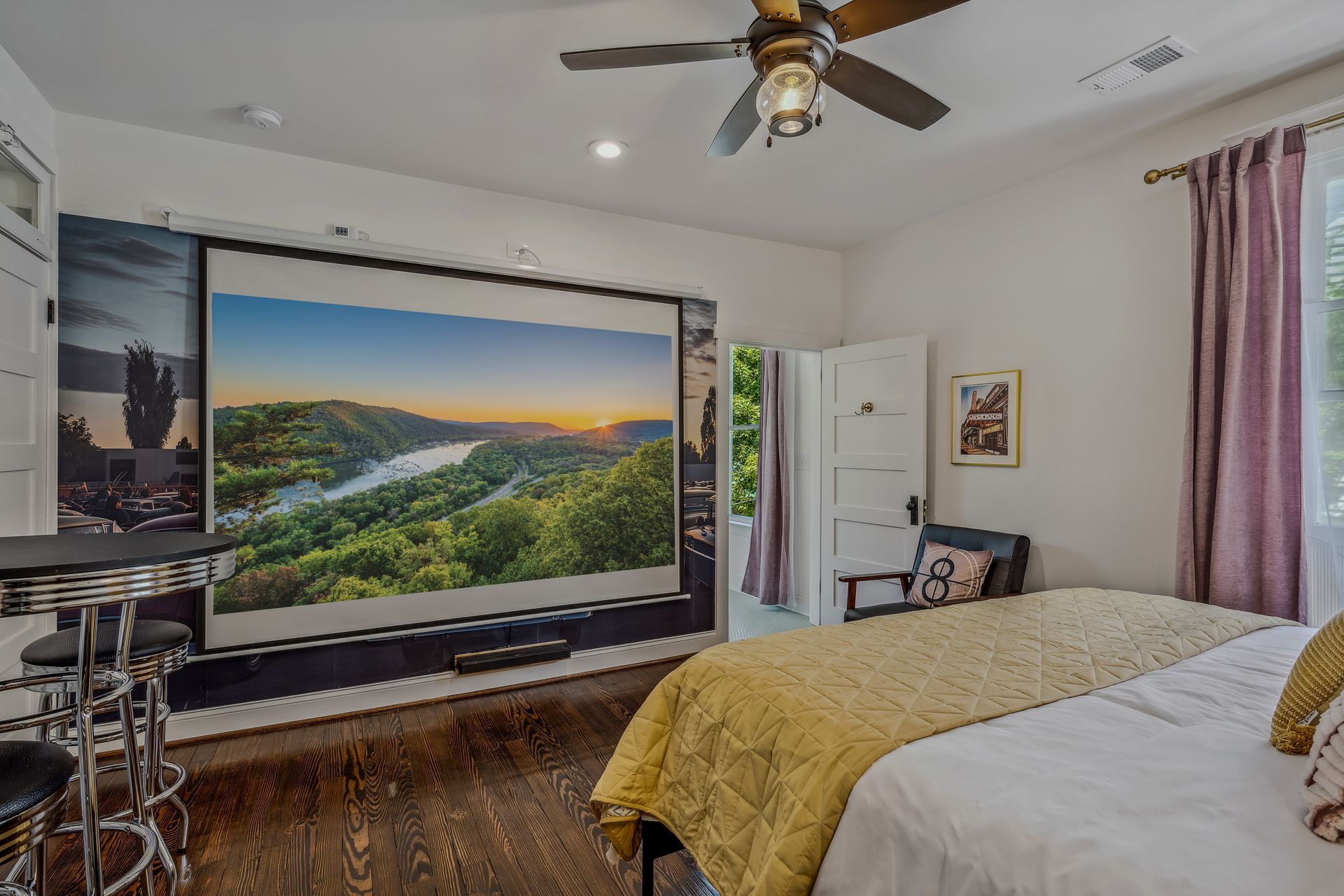 A bedroom with a bed and a large projector screen on the wall.