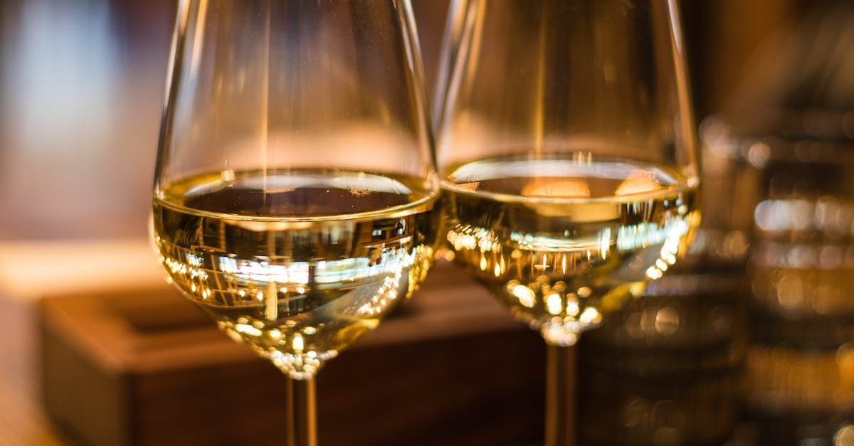 Two glasses of white wine are sitting on a wooden table.