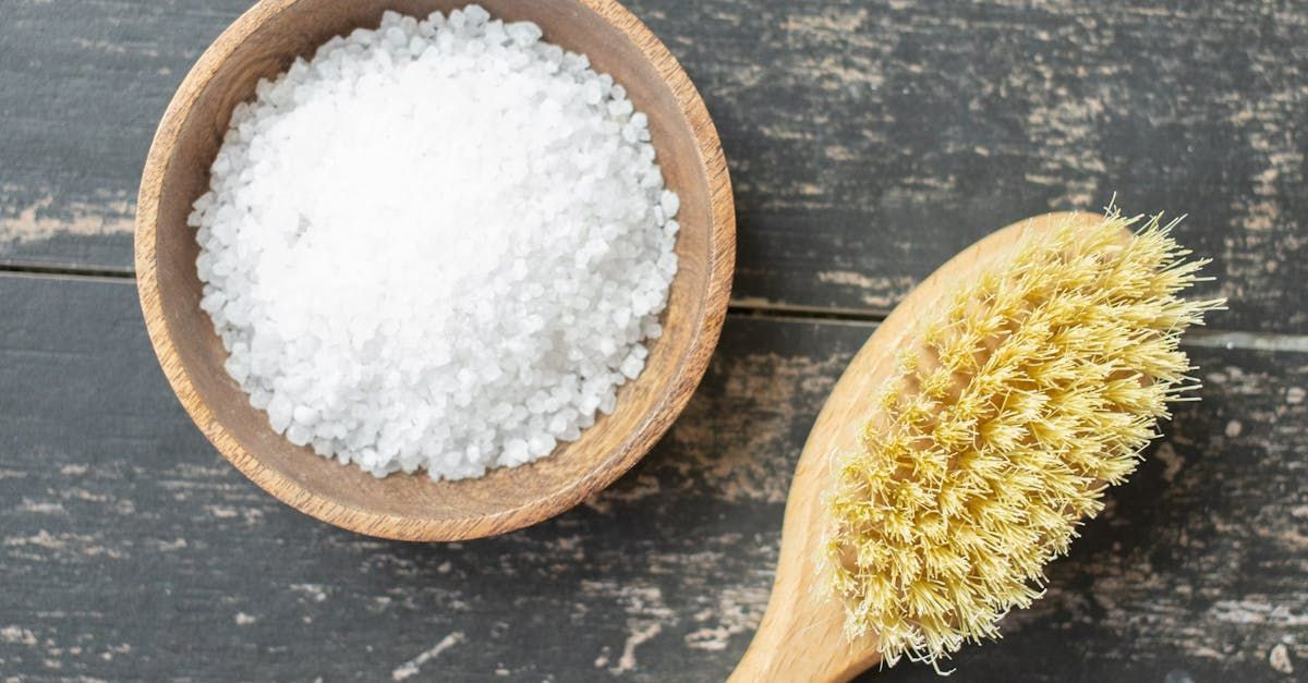 A bowl of salt and a wooden brush on a wooden table.