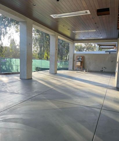 Empty covered patio with concrete floor, wood ceiling, columns, and sunlight streaming in through large windows.