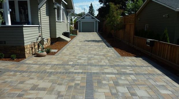 Paved driveway between houses leading to a detached garage, bordered by a wooden fence and garden beds.