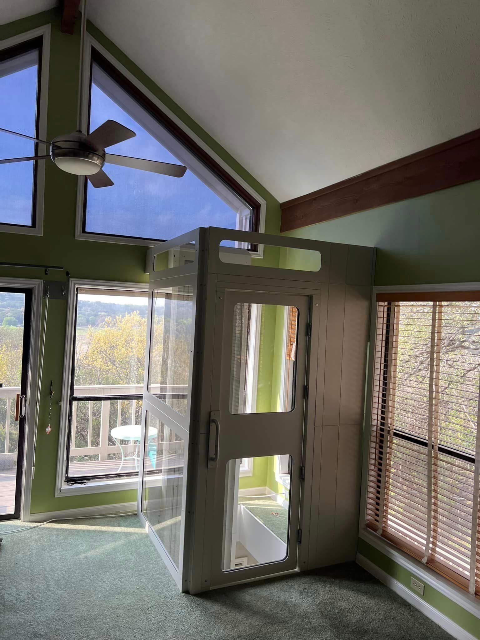 A white, boxy modular shower unit standing in a room with vaulted ceilings, green walls, and large windows.