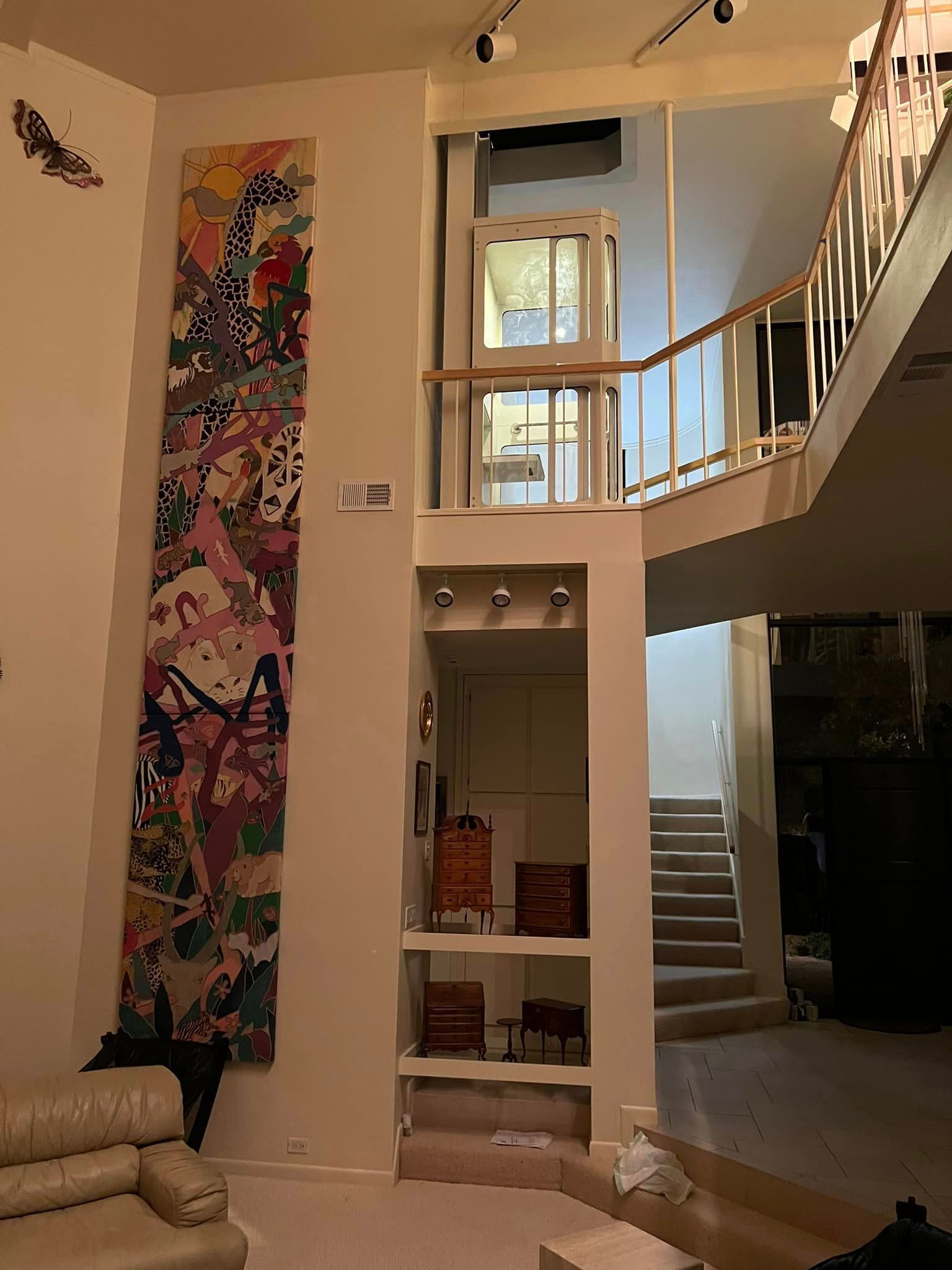 A tall, multi-colored tapestry hangs on a wall in a multi-level residential interior with a staircase and balcony.