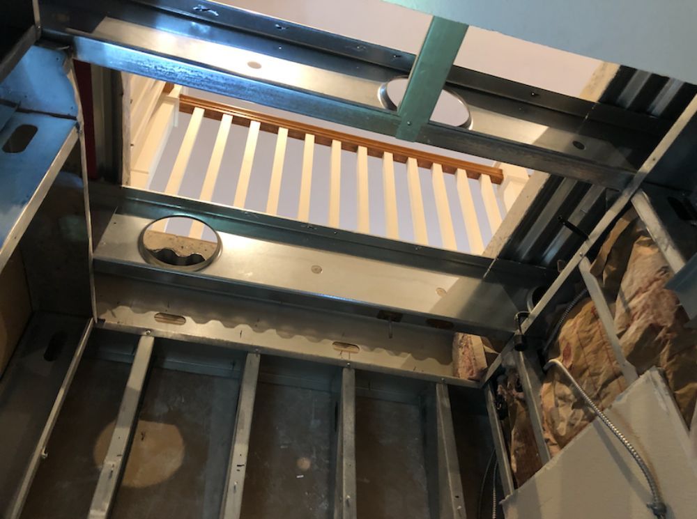 A metal framed wall structure in a room under construction, with a view through the open studs to a white slatted fence.