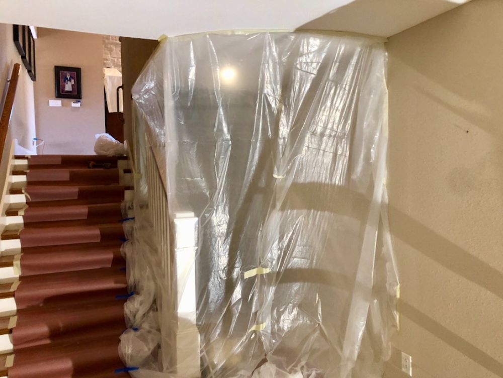 A staircase is covered in brown protective paper, with a plastic sheet hung as a barrier for construction or remodeling.