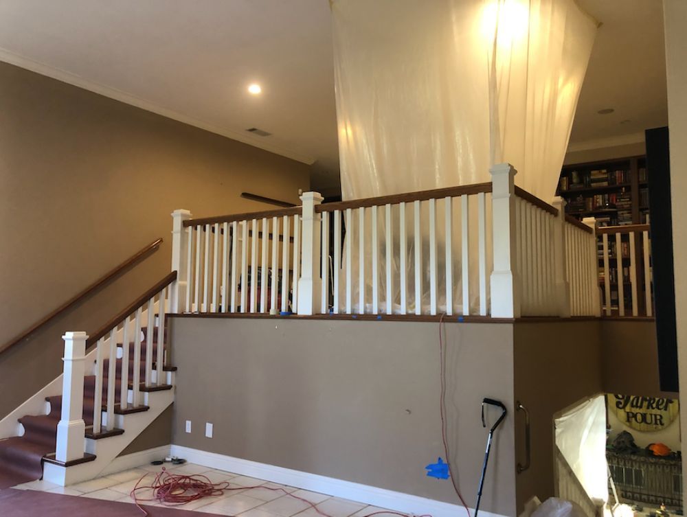 A staircase with white balusters and wood railings leads up to a landing enclosed by plastic sheeting for renovations.