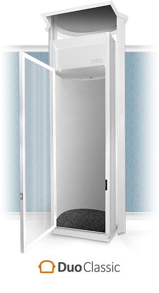 A white DuoClassic residential lift with a transparent door open, positioned against a light blue wall.