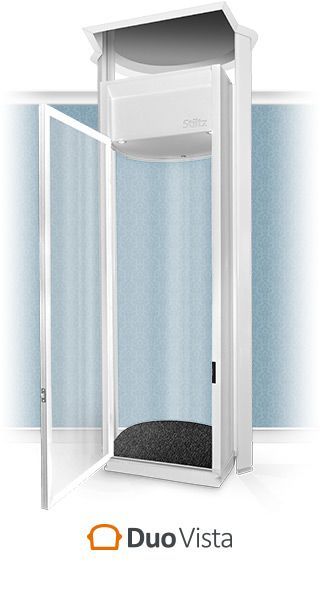 A white, glass-walled Duo Vista home elevator standing against a light blue wall.