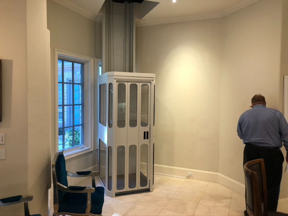 A white residential elevator stands in a room with light walls, tile floors, and a person standing nearby.