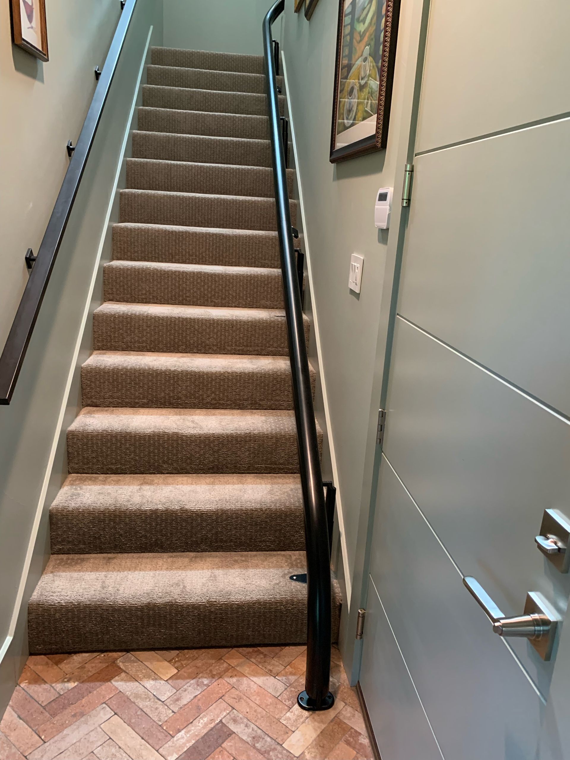 A straight carpeted staircase leading upward, flanked by light green walls, a black handrail, and a door on the right.