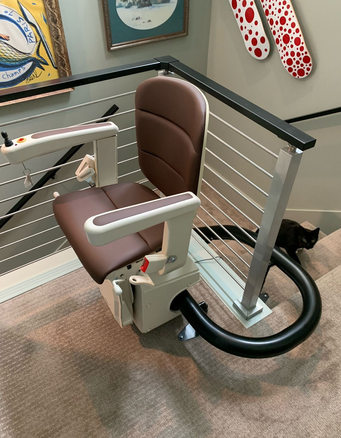 A brown and cream stairlift installed on a staircase, with a black cat sitting on the steps nearby.