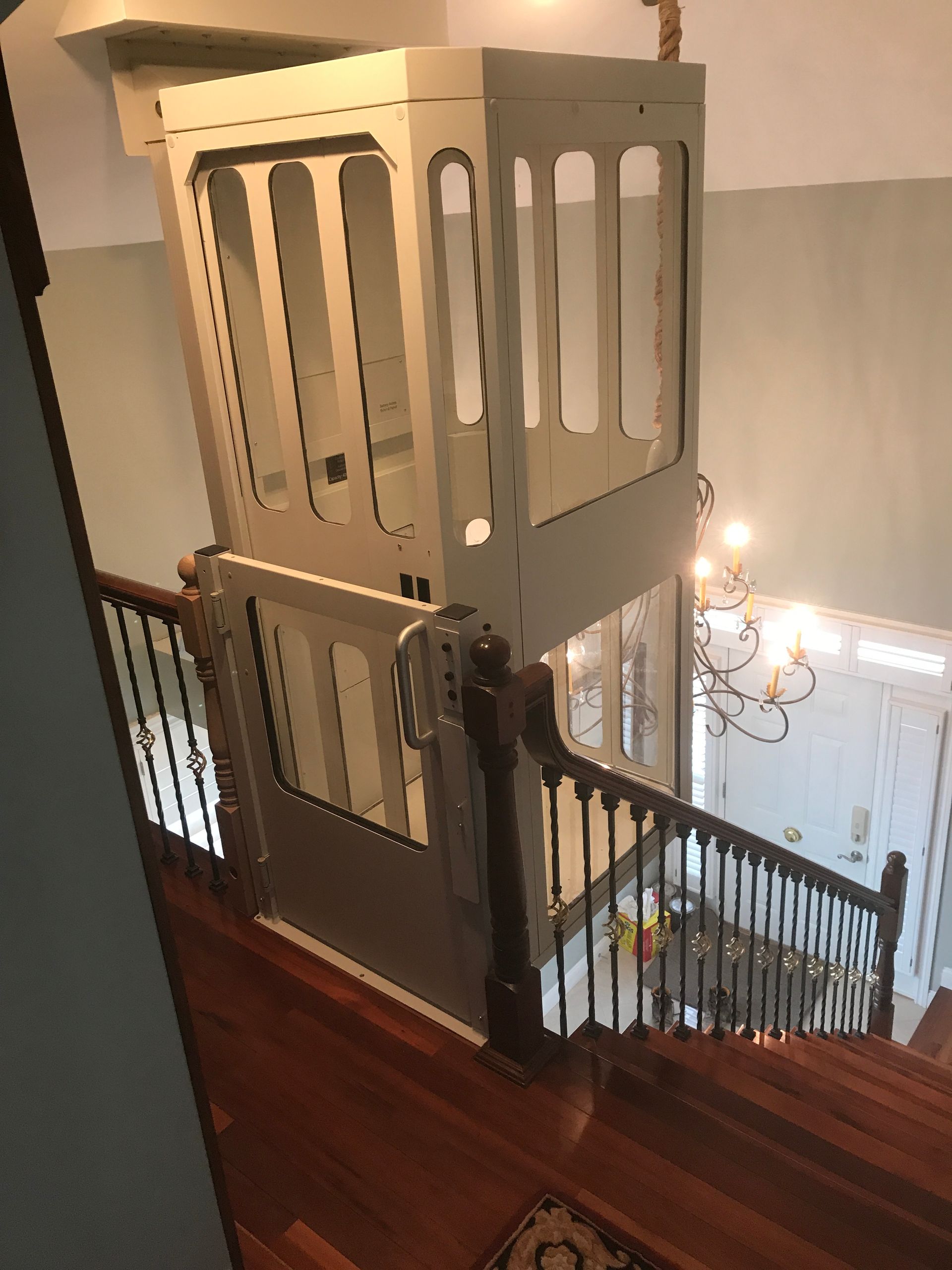 A residential stairlift with a protective enclosure installed at the top of a wooden staircase in a home.