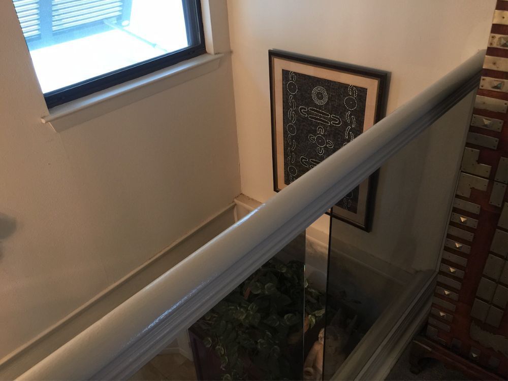A downward-facing view of a staircase featuring a wooden handrail, a framed artwork on the wall, and a window above.