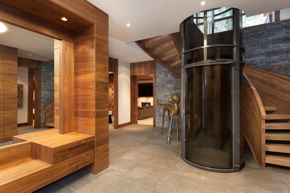 A contemporary entryway featuring wooden walls, stone flooring, a spiral staircase, and a cylindrical glass elevator.