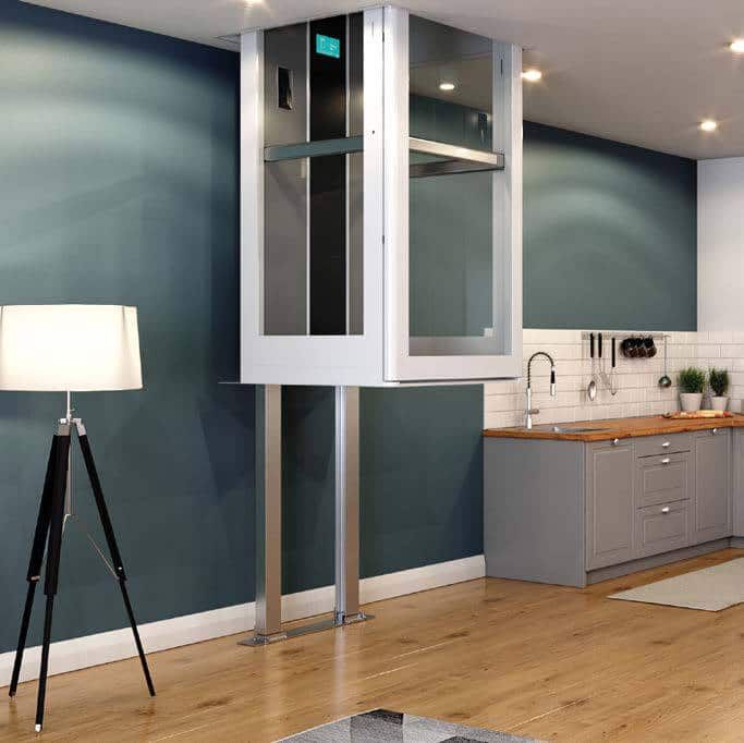 A residential elevator installed in a kitchen, featuring a modern white frame, glass panels, and vertical guide rails.