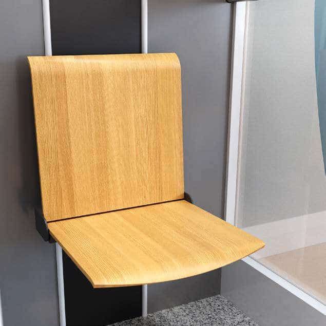 A wall-mounted, fold-down wooden shower seat with a backrest installed against a grey wall.