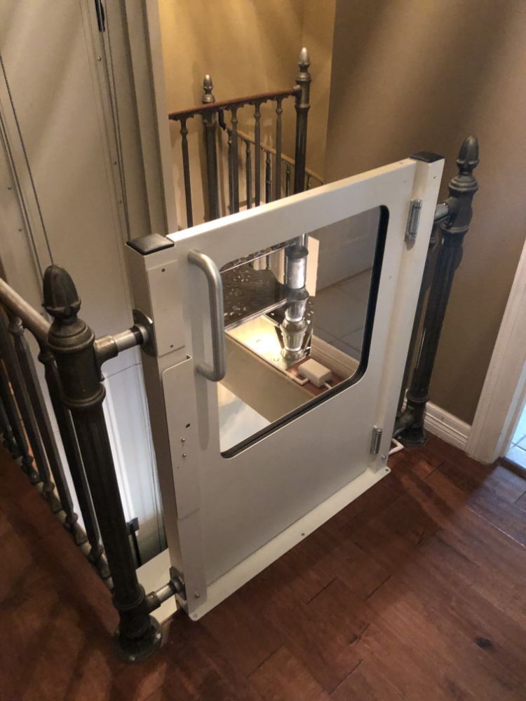 A white child safety gate with a transparent center panel installed at the top of a wooden staircase.