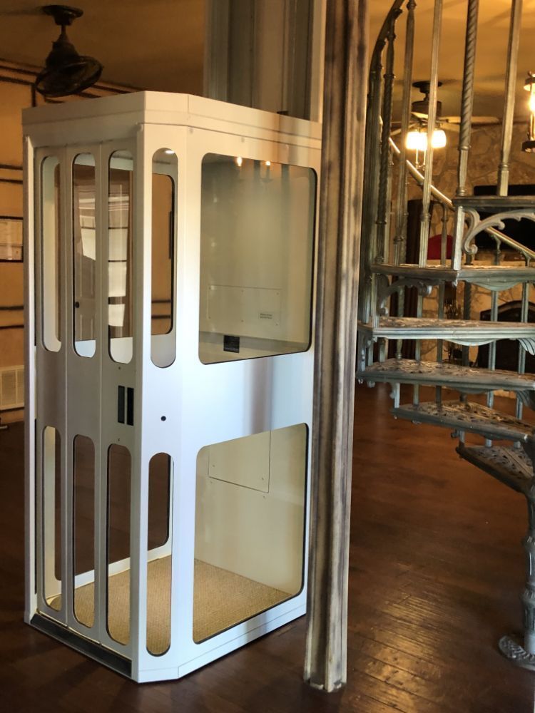 A residential elevator with white framing and glass windows positioned next to a wrought-iron spiral staircase.