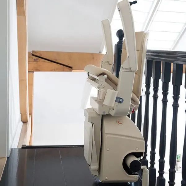 A brown and white stairlift mounted on a curved rail in a home with a wooden floor and a green potted plant nearby.