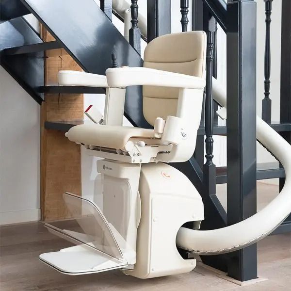 Cream-colored stairlift mounted on a black wooden staircase, featuring a padded seat, armrests, and footrest.