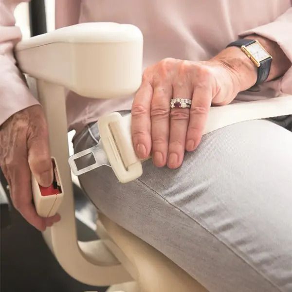 A person's hands securing a beige safety seatbelt on a chair by inserting the metal buckle into the red release clasp.