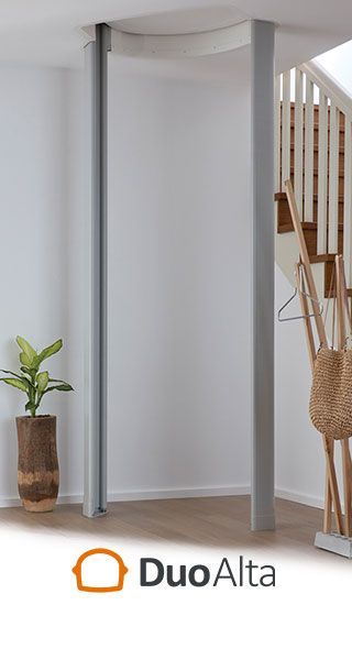 A curved gray privacy screen track installed on a white ceiling next to a staircase and a potted plant, with DuoAlta logo.
