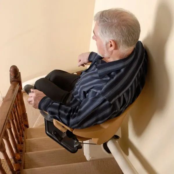 A Legacy II stairlift with a beige seat and armrests installed on a track, featuring a wireless remote control.