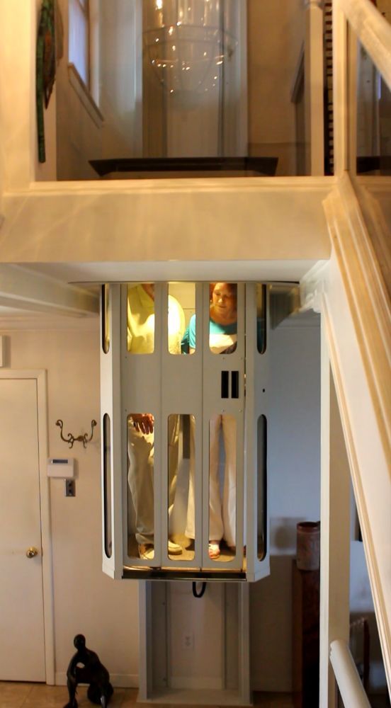 A person stands inside a small, white residential elevator moving between the floors of a home.