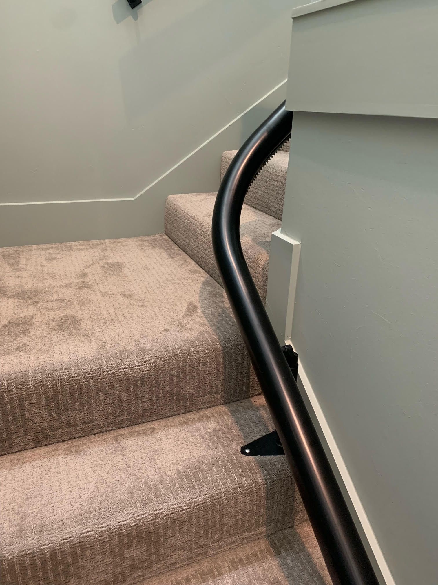 A black, curved handrail attached to a wall next to carpeted stairs in a residential interior.