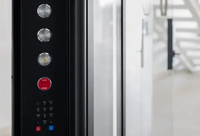 Elevator panel with up and down buttons, speaker grille, and red emergency stop button with wireless signal icon