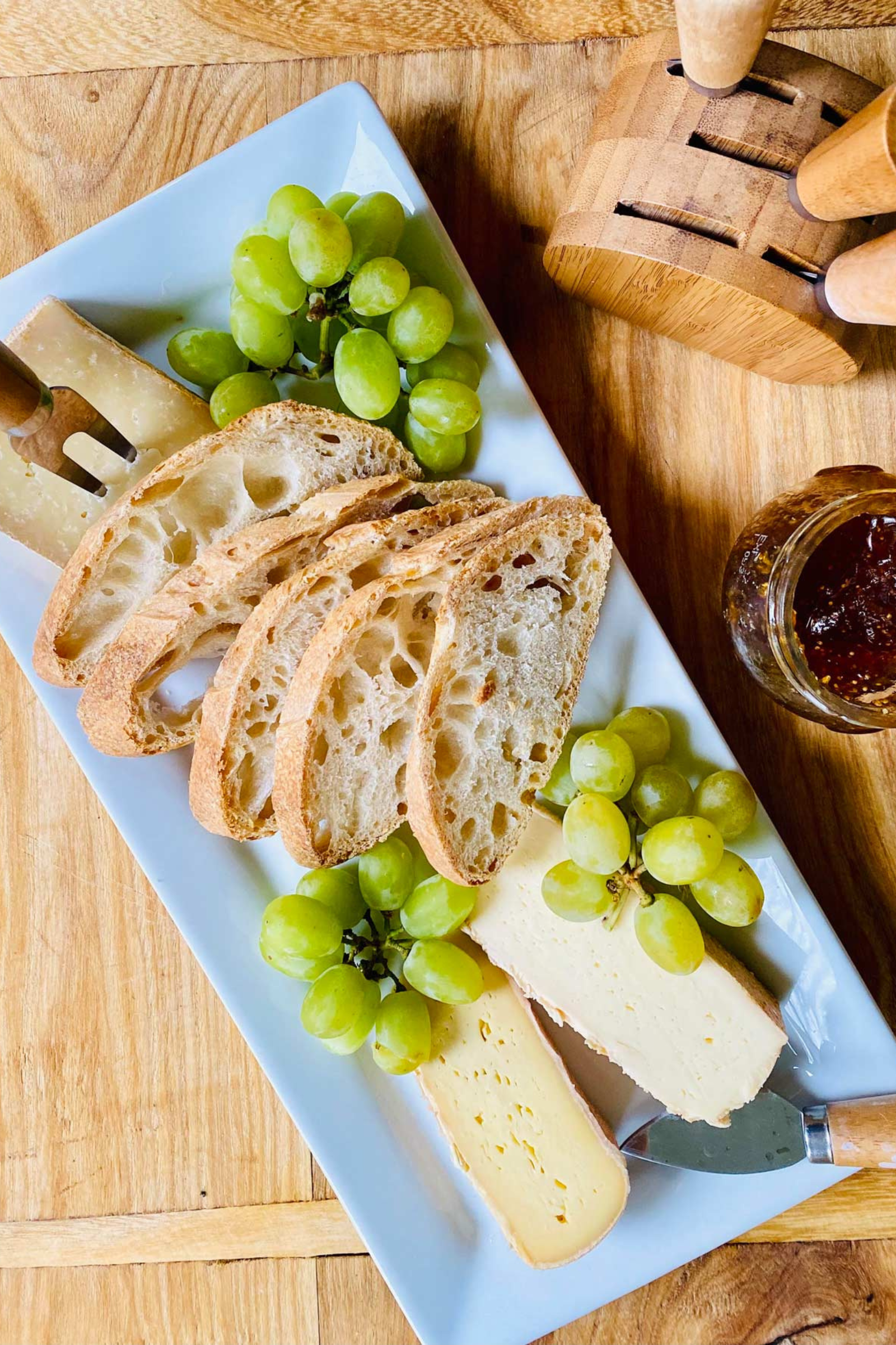 A white plate topped with bread , cheese , and grapes on a wooden table.