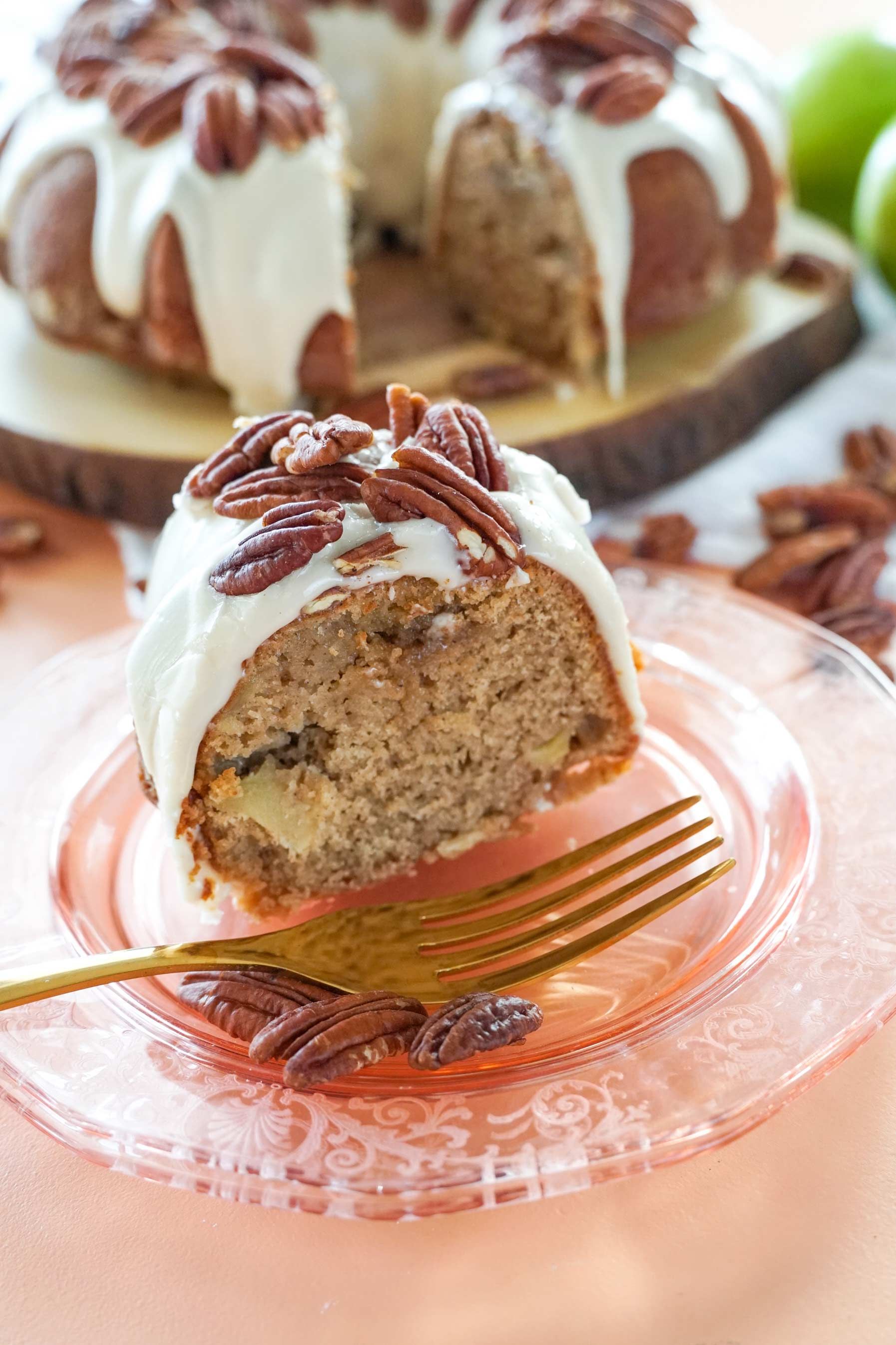 A bundt cake with pecans on top is on a plate with a fork.