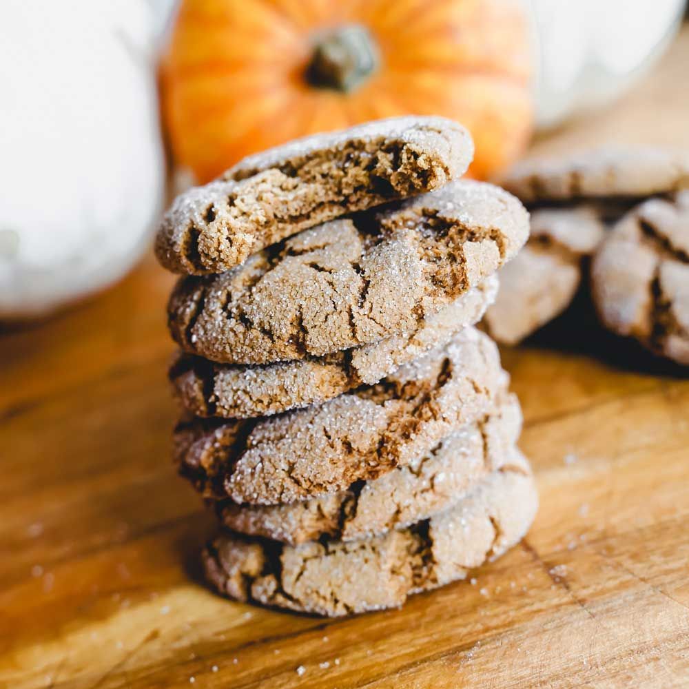 A stack of cookies on a wooden table with a pumpkin in the background.