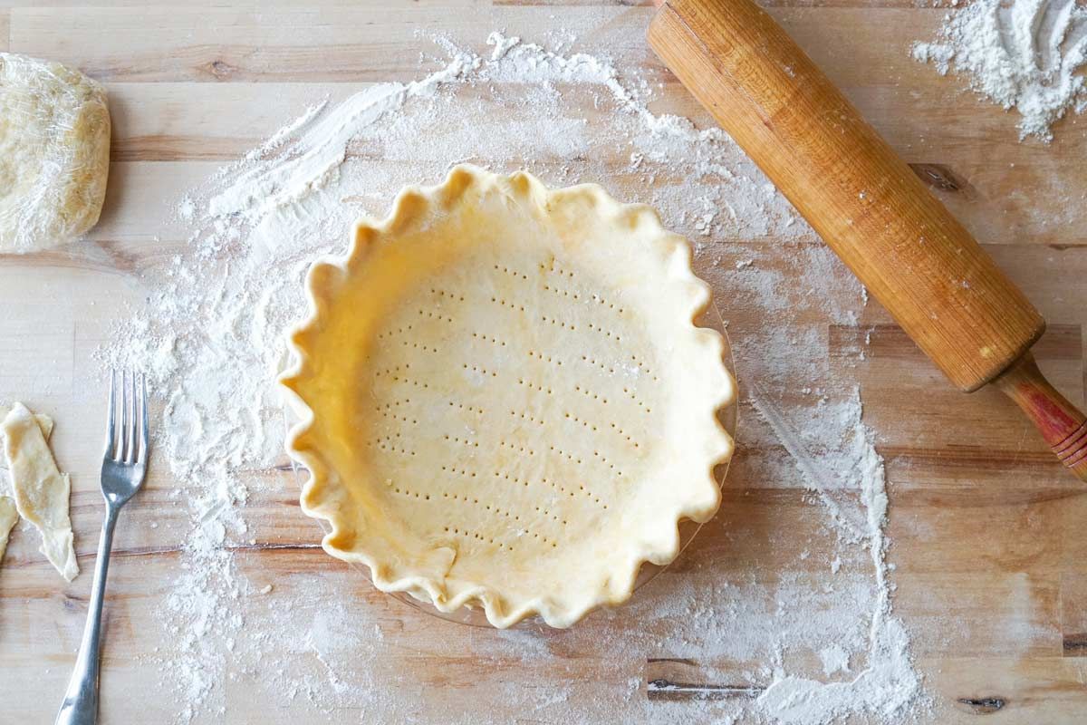 A pie crust is sitting on a wooden table next to a rolling pin.