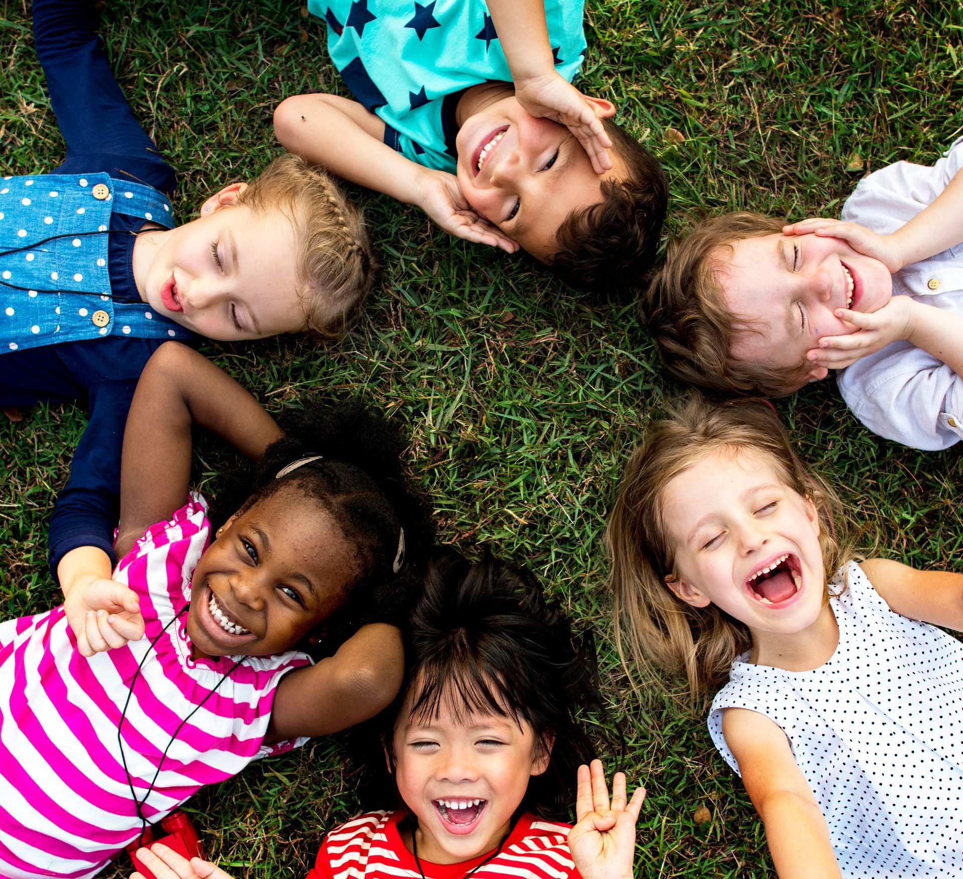Group of children lying in green grass, smiling and laughing together