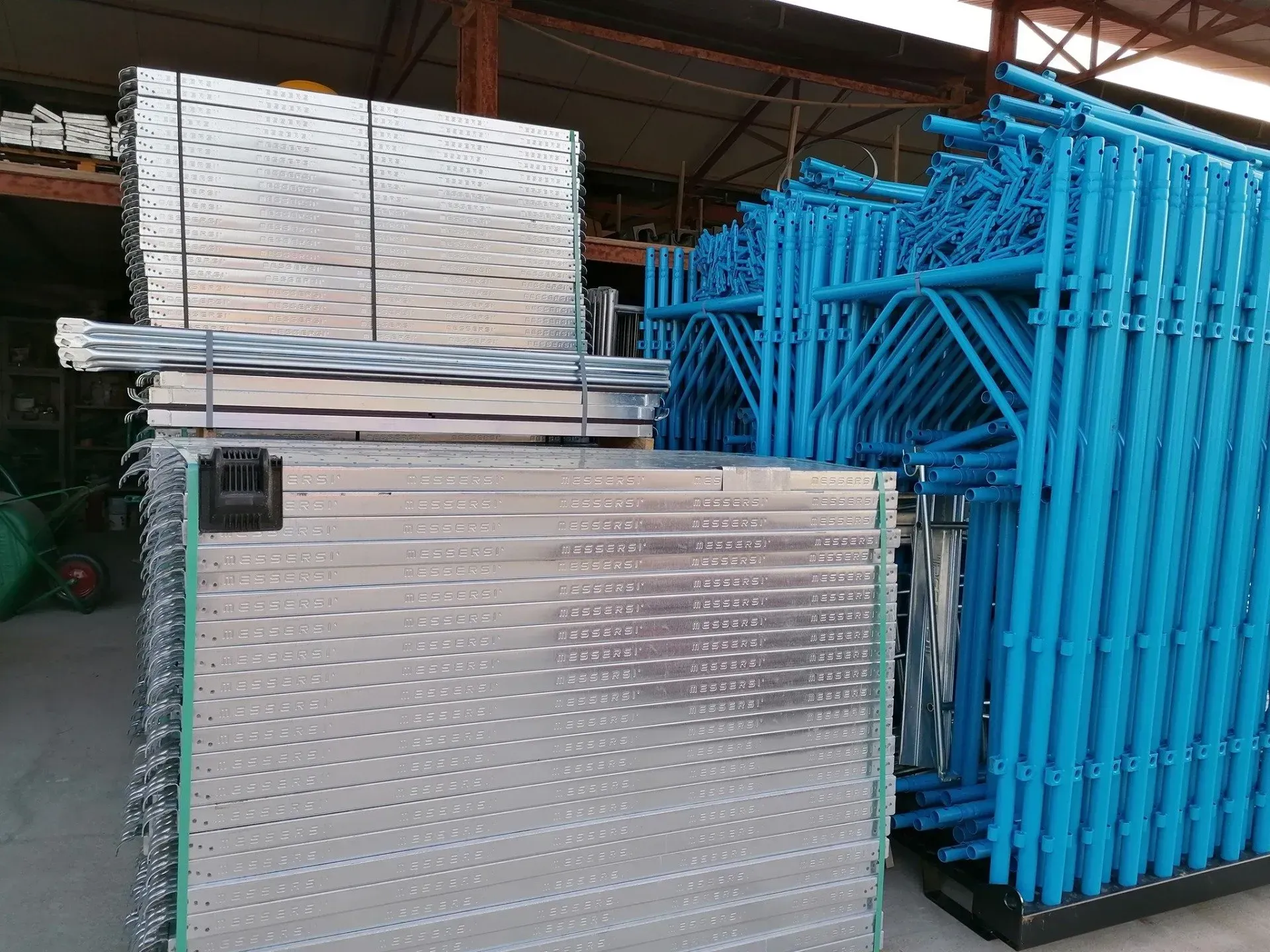 Pile di pannelli di scaffalatura in metallo blu in un magazzino, con materiali imballati accanto.