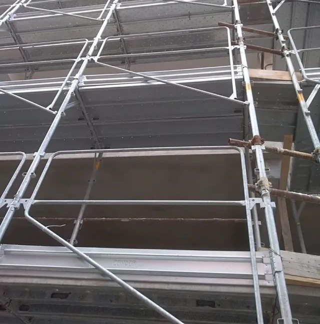 Impalcatura attorno alla facciata di un edificio con pali e traverse metalliche contro un muro grigio