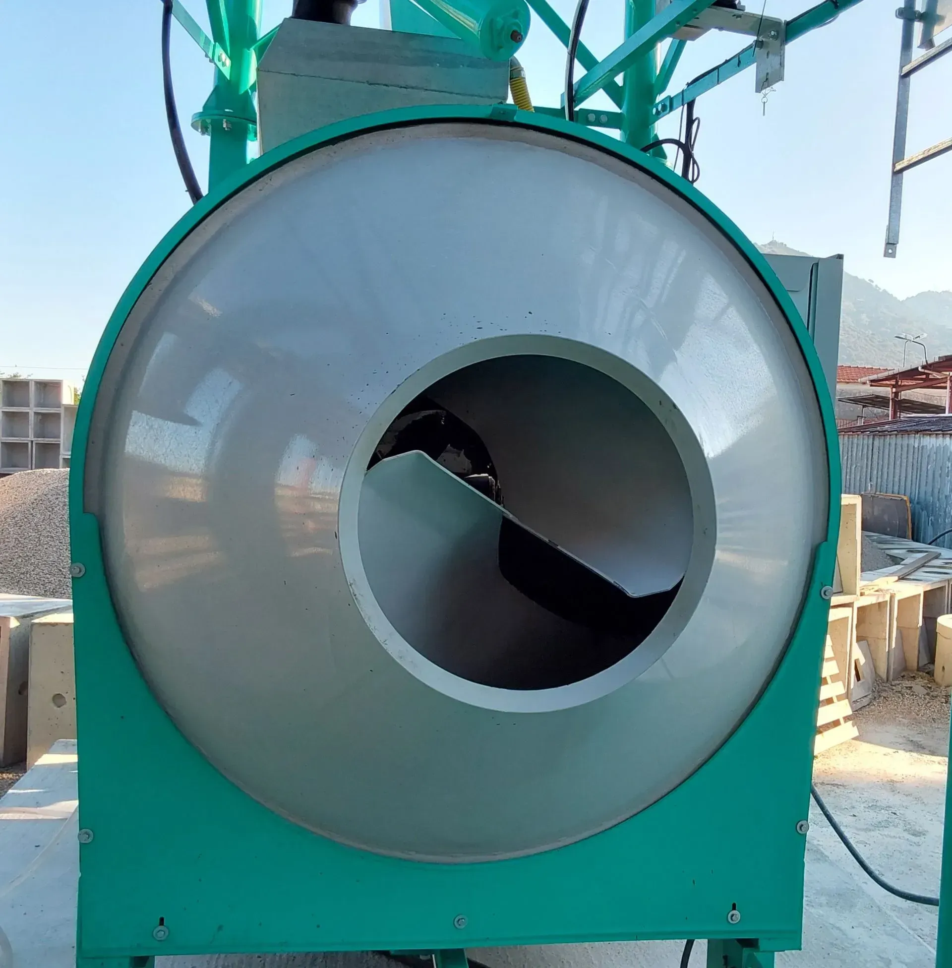 Macchina industriale color verde acqua con scivolo circolare argentato, posizionata all'aperto in un cantiere.