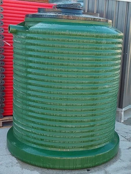 Grande serbatoio o contenitore cilindrico verde a coste, posizionato all'esterno, su uno sfondo rosso ondulato.